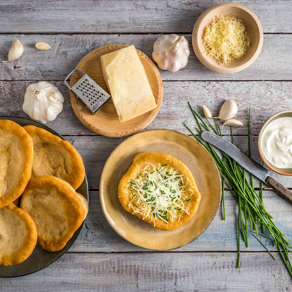 Traditionelle ungarische Langos mit Knoblauch, Käse und Sauerrahm, garniert mit gehacktem Schnittlauch, Draufsicht