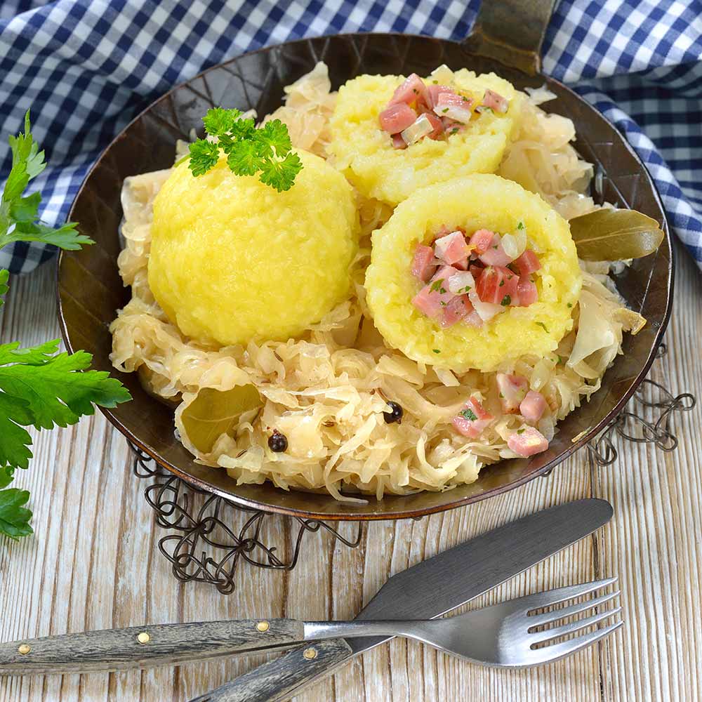 Mit Südtiroler Speck gefüllte Kartoffelknödel auf Sauerkraut im Eisenpfandl serviert